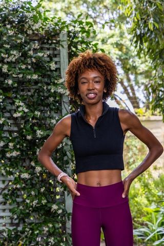 African american woman posing in garden wearing crop top, leggings and smartwatch
