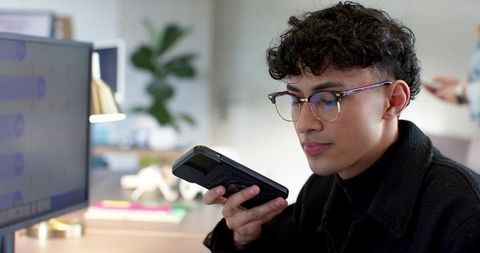 Young professional speaking into handheld recorder at office desk during team collaboration