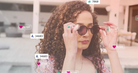 Curly woman adjusting round sunglasses poolside with social media likes influencer style
