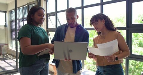 African american team collaborating around laptop with documents in sunlit office