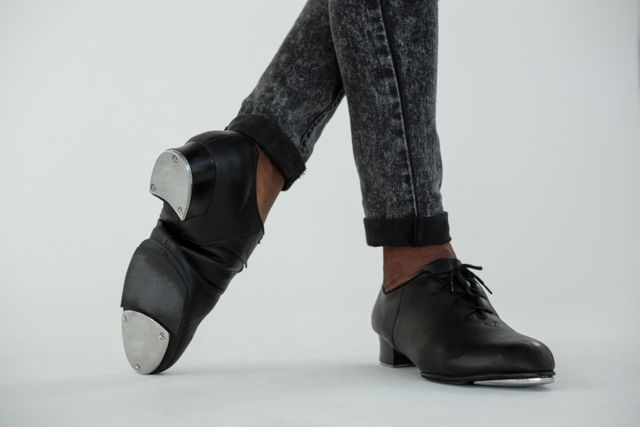 Close-up of a tap dancer's feet wearing black tap shoes and jeans, practicing in a dance studio. Ideal for use in articles about dance, performing arts, dance education, and cultural activities. Suitable for promoting dance classes, workshops, and dancewear products.