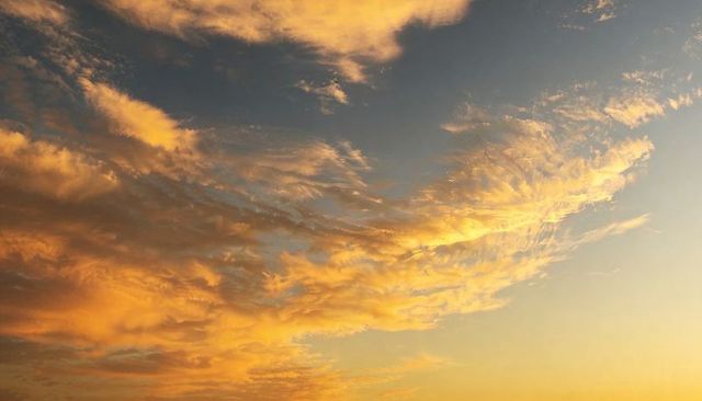 Golden Clouds Glowing Over Sunset Horizon with Wispy High Clouds and Textured Amber Sky