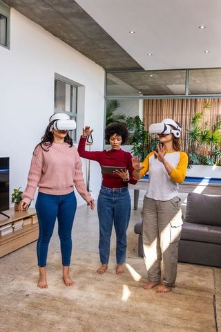 Multicultural women experiencing virtual reality at home lounge with tablet guidance
