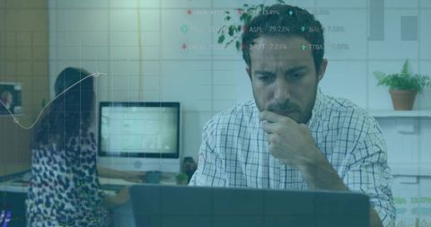 Man analyzing translucent data overlays on laptop while colleague typing in shared office