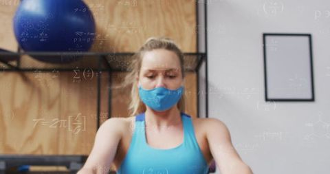 Masked woman working out in studio wearing blue tank with stability ball, focused fitness