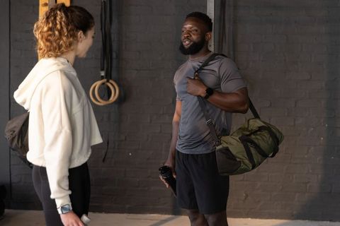 Diverse training partners chatting after workout with duffel bag and shaker bottle