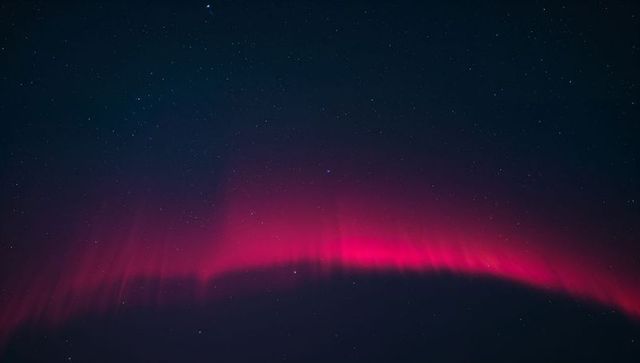 Magenta aurora arc dancing across starry night sky over dark horizon