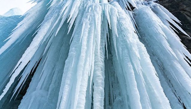 Cascading icicle columns forming on cliff face, towering frozen waterfall stalactites