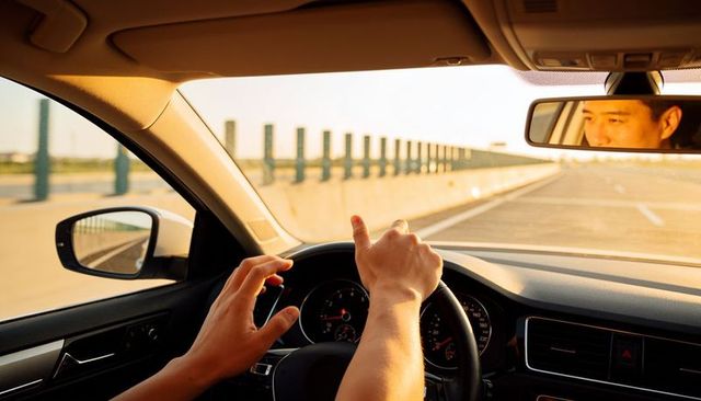 Hands steering car on sunlit bridge during golden hour commute