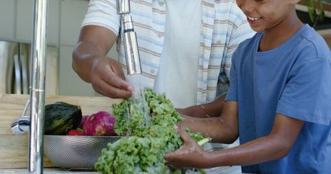 African american father and son washing kale and vegetables at kitchen sink