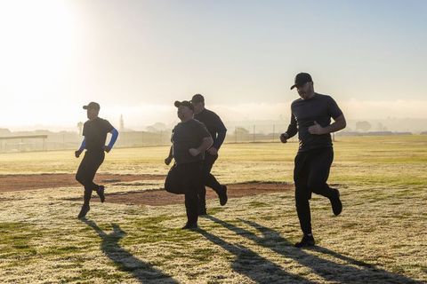 Sunlit dawn group running drill on dewy grass field with caps and dark athletic clothing