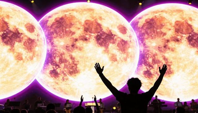Silhouette fan raising arms at live concert with triple giant moon projection and neon lights