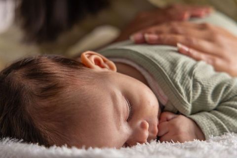 Sleeping infant receiving gentle caregiver touch, green onesie close-up bonding moment