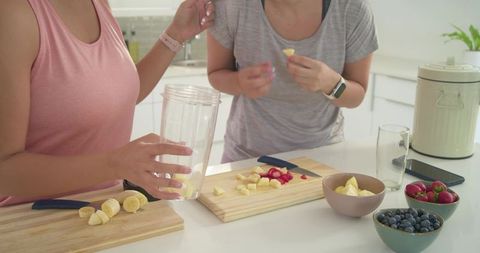 Two women preparing fresh fruit smoothies on bright modern kitchen countertop