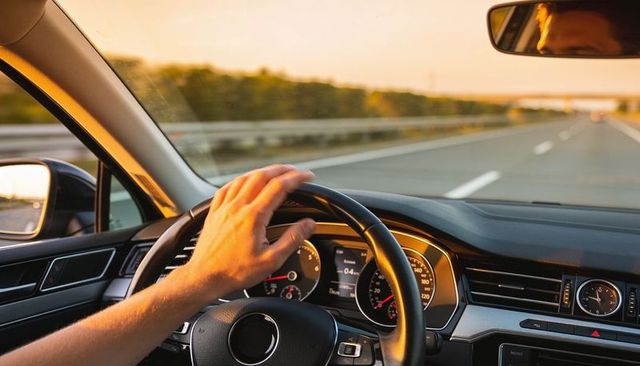 Sunset highway driving with hand on steering wheel and glowing dashboard display