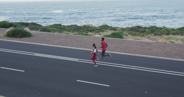 Two individuals running along a road adjacent to the ocean, demonstrating a healthy lifestyle and outdoor physical activity. Ideal for promoting fitness, wellness programs, outdoor sports, and scenic coastal activities.