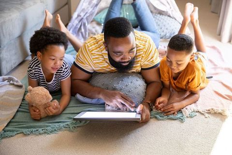 Father Bonding with Children Under Blanket Fort Using Tablet