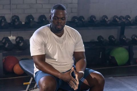 Sitting and rubbing chalk after heavy lifting, focused african man on gym bench