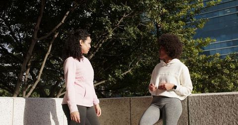 Two Women Chatting During Outdoor Fitness Break on Urban Terrace with Smartwatch