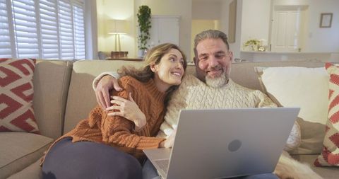 Happy Couple Enjoying Relaxed Evening with Laptop on Sofa at Home