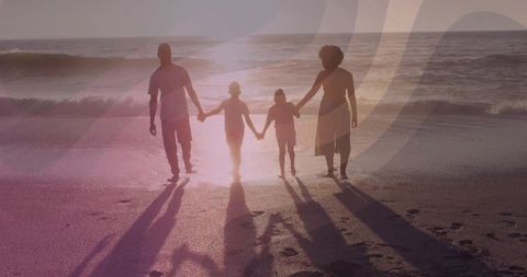 Sunset family silhouettes walking hand in hand along shoreline with long dramatic shadows
