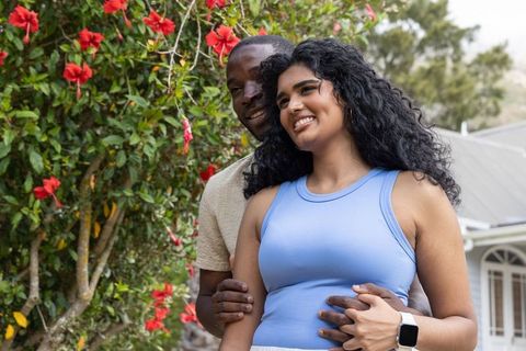 Sunlit diverse couple embracing in garden with hibiscus blooms and casual summerwear