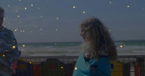 Two girls wrapped in towels on seaside promenade facing each other with golden sunlit bokeh
