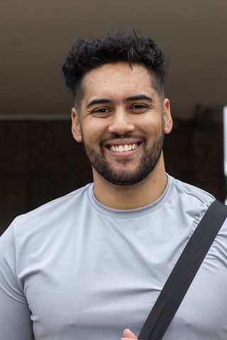 Smiling african american man with beard in light gray shirt carrying backpack over shoulder