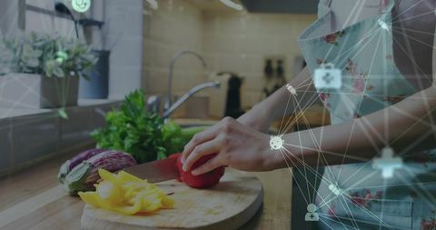 Floral-apron woman slicing red bell pepper on wooden board with smart network overlay
