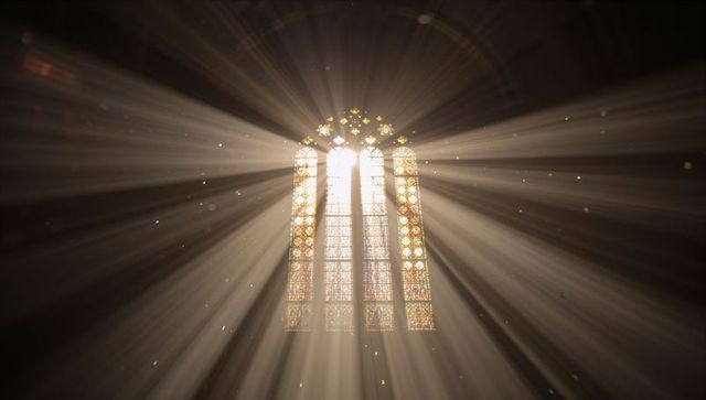 Golden sunbeams streaming through gothic lancet stained-glass window in cathedral nave