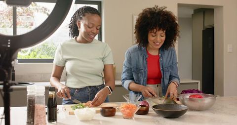Diverse women chopping vegetables and assembling healthy meal at modern kitchen island