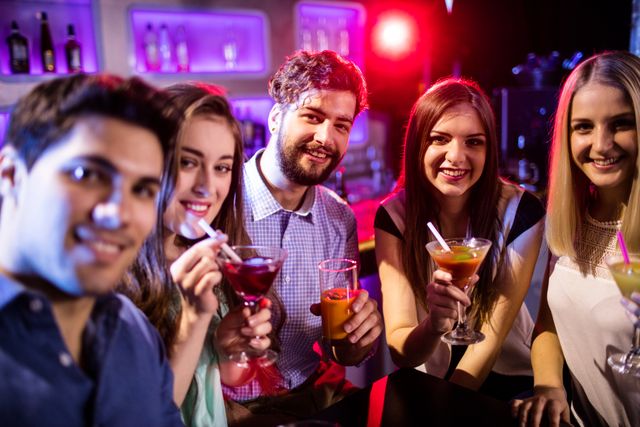 Portrait of smiling friends having cocktail at bar counter in bar