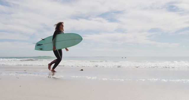 Image captures a young surfer walking along a tranquil beach, holding a surfboard under a clear, bright sky. Waves appear softly in the background, indicating a peaceful day perfect for surfing. This image can be used in contexts related to beach culture, surfing lifestyle, outdoor activities, summer vacations, and beach sports promotions.