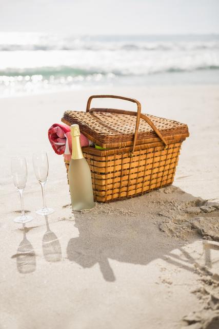 Picnic basket, champagne bottle and two glasses at tropical sand beach