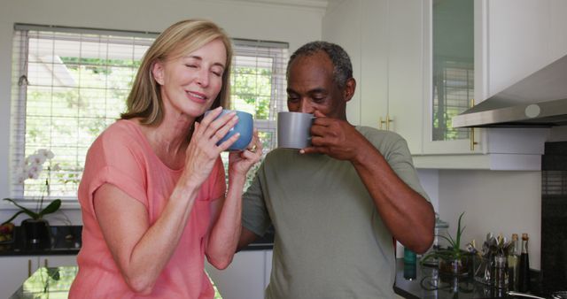 Happy diverse senior couple drinking coffee and talking standing in kitchen. staying at home in isolation during quarantine lockdown.