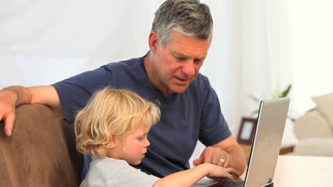 Grandfather and Grandson Engaged with Laptop Together at Home
