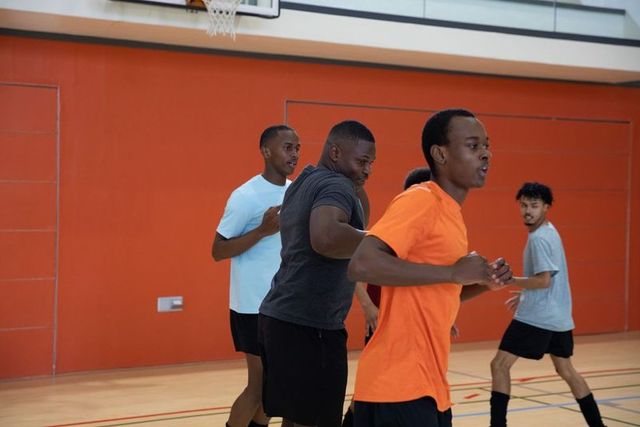 Young black men sprinting in indoor basketball practice near bold orange court wall