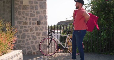 Mid-adult man standing at stone entrance with bicycle and red jacket, casual lifestyle