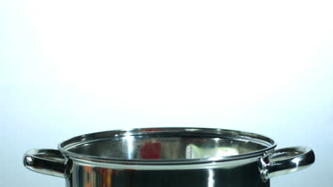 Red Chili Pepper Falling into Shiny Metal Pot in Slow Motion