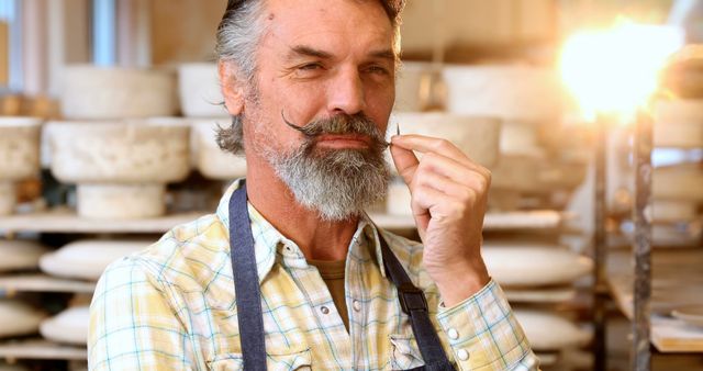 A mature artisan with a twirled mustache in a cheese workshop. He wears an apron, exuding confidence in his craft. This can be used in articles, advertisements, and websites focusing on skilled trades, craftsmanship, artisanal food production, and profiles of professionals.