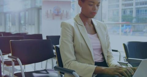 Businesswoman working on laptop in modern glass lobby during daytime, professional urban workspace