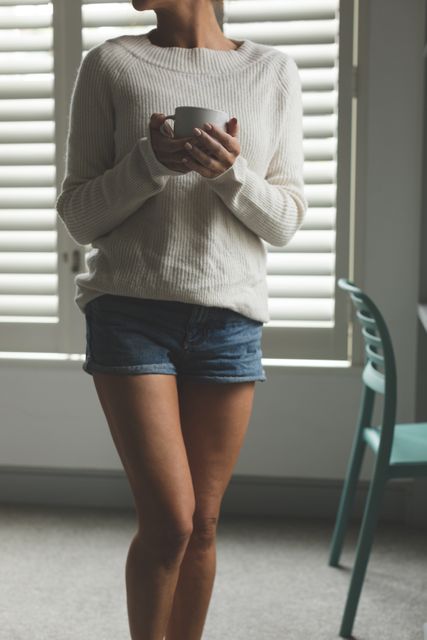 Mid section of woman standing in living room while having coffee in a comfortable home