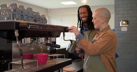 Baristas steaming milk and pulling espresso at commercial machine, teamwork and training