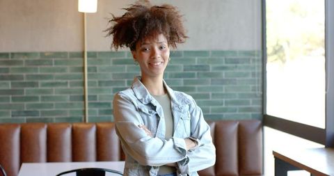 Confident african american woman standing with arms crossed in modern cafe interior