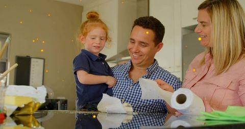 Smiling family cleaning kitchen together holding child on countertop with paper towel roll