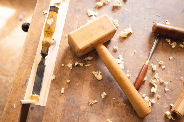 High angle view of a wooden mallet, chisel, and other hand tools on a workbench covered with wood shavings. Ideal for illustrating concepts related to woodworking, carpentry, craftsmanship, and handmade manufacturing. Suitable for use in articles, blogs, and advertisements focusing on DIY projects, woodworking tutorials, and craftmanship.