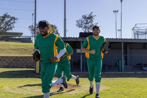 Community baseball teammates running from dugout in green and yellow uniforms, smiling