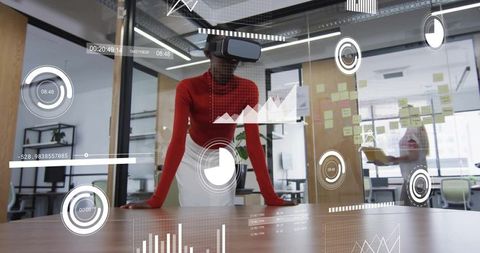 Businesswoman wearing vr headset leaning on desk displaying ar hud charts and graphs in office