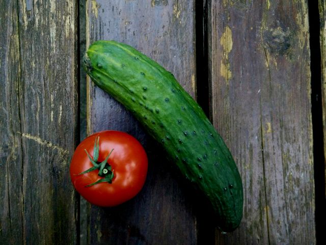  Fresh tomato and cucumber on a rustic wooden table, with natural lighting creating a vibrant and appetizing look. Ideal for use in food blogs, recipe websites, marketing materials for farm produce, and health-focused articles.