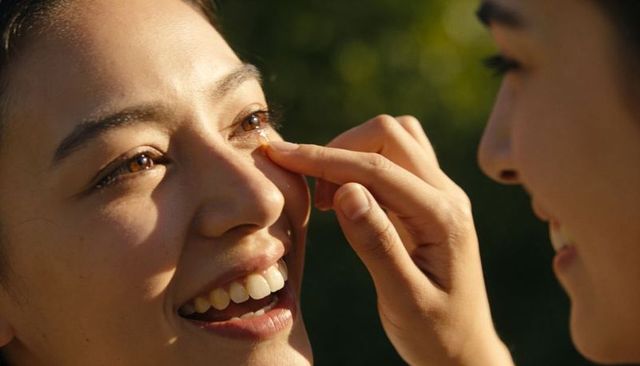 Tender fingertip wiping tear while smiling partner shares sunlight close-up